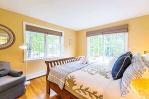 Ein Schlafzimmer mit Bett, zwei Fenstern, einem Sessel und einer Lampe.