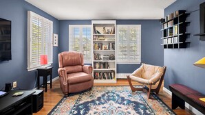 A room with a brown leather chair, a beige chair, a bookshelf, and a television on a black stand. - Close to Bike Path 1 Mile to Beaches! (South Chatham)