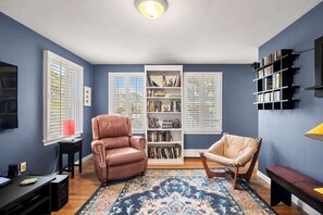 A room with a brown leather chair, a beige chair, a bookshelf, and a television on a black stand. - Close to Bike Path 1 Mile to Beaches! (South Chatham)