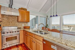 A modern kitchen with a stainless steel stove, wooden cabinets, granite countertops, and a view of the city through large windows.