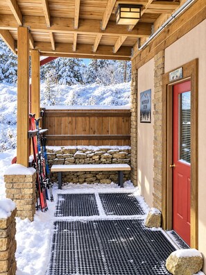A wooden covered entrance with a bench, a stone wall, a red door, and a sign for the Mountain Crew. - BEST 6br Ski-In+Out w. Hot Tub->Gear rm, PS-5, Fun+Lux (Snowshoe)