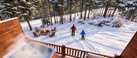 A snow-covered outdoor area with a hot tub, wooden deck, and a fire pit.