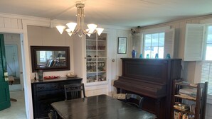 Un comedor con una mesa y sillas de madera, un piano, una estantería y un aparador con puertas de vidrio.