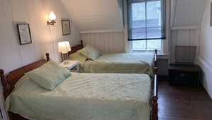 Un dormitorio con dos camas, una mesita de noche, una lámpara, una ventana con persianas y un baúl de madera.