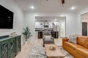 Ein modernes Wohnzimmer mit Flachbildfernseher, einer Ledersofa, einem Couchtisch und einem Essbereich mit Küche im Hintergrund.