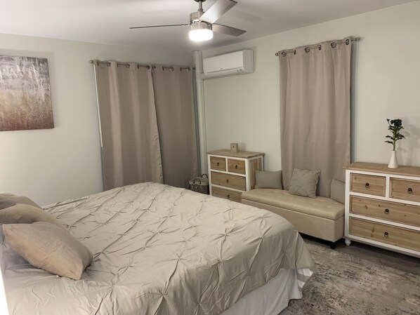 A bedroom with a bed, bedside tables, a dresser, a ceiling fan, and curtains.