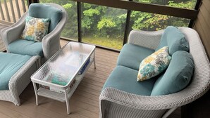 Ein Balkon mit Korbmöbeln und einem Glastisch, mit Blick auf einen üppigen, grünen Wald.