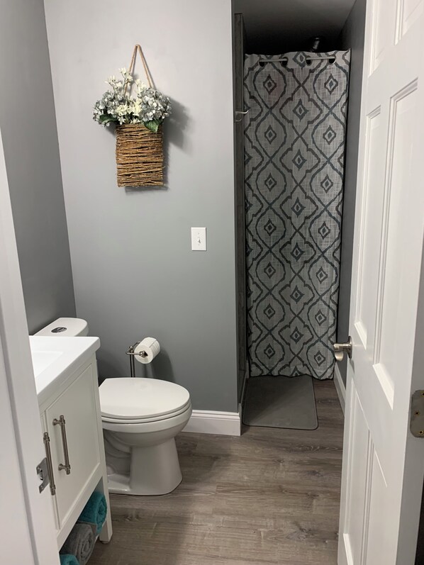 A bathroom with a toilet, a sink, a basket of flowers, and a shower curtain.