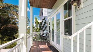 A wooden deck with a white railing, a covered porch, and a view of a building with a white exterior and a balcony. - Fish Stix: Elevator, 4 Houses to Beach, Pool by Anna Maria Life Vacation Rentals (Holmes Beach)