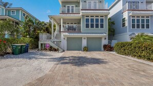 A two-story house with a covered driveway, a front porch, and a garage. - Fish Stix: Elevator, 4 Houses to Beach, Pool by Anna Maria Life Vacation Rentals (Holmes Beach)
