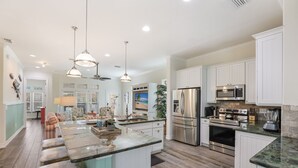 A spacious kitchen with a central island, stainless steel appliances, and a large island with bar stools. - Fish Stix: Elevator, 4 Houses to Beach, Pool by Anna Maria Life Vacation Rentals (Holmes Beach)