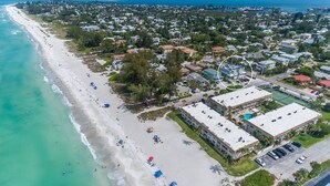 An aerial view of a coastal town with a beach, residential buildings, and a large hotel with multiple floors and a parking lot. - Fish Stix: Elevator, 4 Houses to Beach, Pool by Anna Maria Life Vacation Rentals (Holmes Beach)