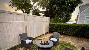 Un patio con un pozo de fuego, cuatro sillas de mimbre y una valla de madera.