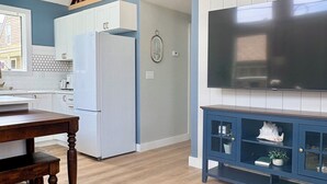 Cocina moderna con armarios blancos, una escalera de madera, un televisor de pantalla plana y un mueble azul decorado con objetos.