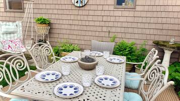 An outdoor patio with a table set for dining, surrounded by white wicker chairs and cushions.