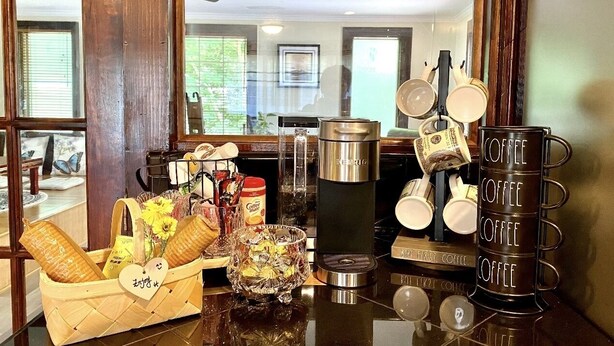 Una estación de café con cafetera, tazas y una cesta de bollería.