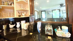 Una cocina con encimera negra, una licuadora, una cafetera, un tostador y una cesta con productos de limpieza.