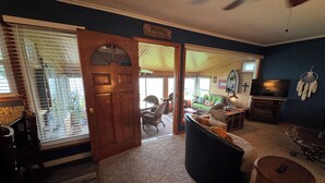Un salon chaleureux avec une porte en bois, un pouf noir, un téléviseur et un ventilateur de plafond.