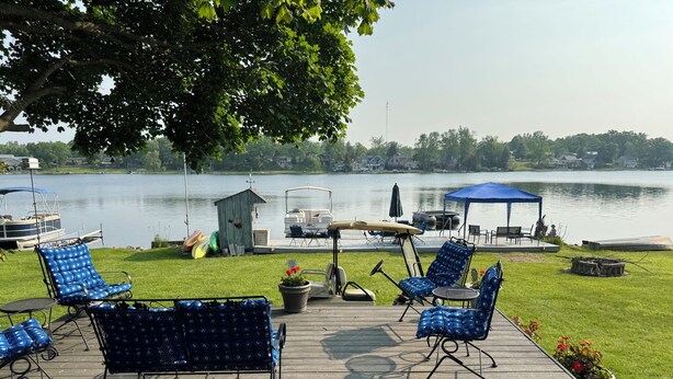 Une terrasse avec des chaises à motifs bleus et une table, donnant sur un lac où l’on peut voir des bateaux et un quai.
