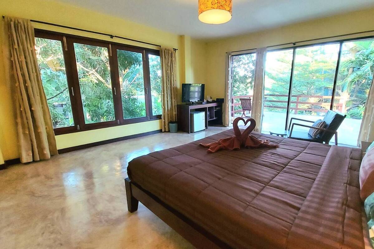 Une chambre spacieuse avec un grand lit, une télévision et un balcon offrant une vue sur la verdure.