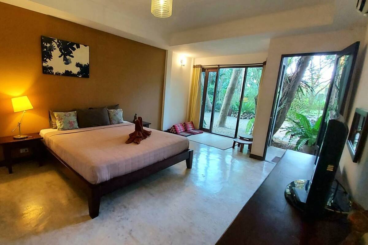 Une chambre d’hôtel moderne dotée d’un grand lit, d’une lampe de chevet, d’un téléviseur à écran plat et offrant une vue sur la verdure grâce à une grande porte-fenêtre coulissante.