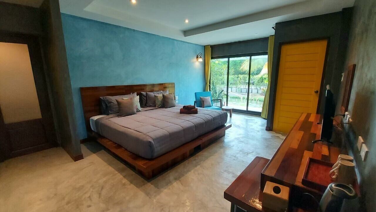 A modern bedroom with a large bed, a wooden bench, and a view of the outdoors through a large window.