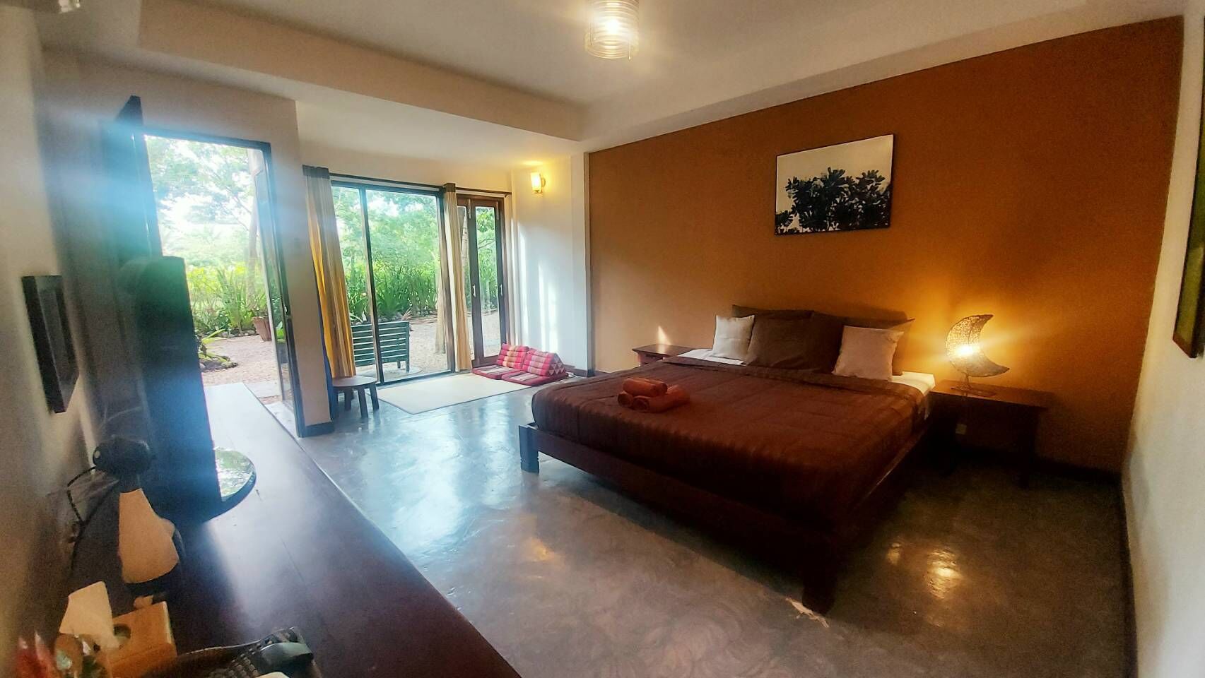 Habitación de hotel con una cama grande, un escritorio con silla, televisión y puerta corrediza de vidrio que da a un área exterior.