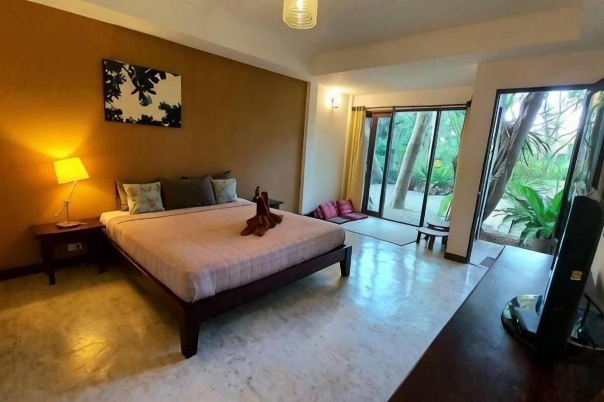 Une chambre à coucher avec un lit, une table de chevet, une lampe et une vue sur l’extérieur.