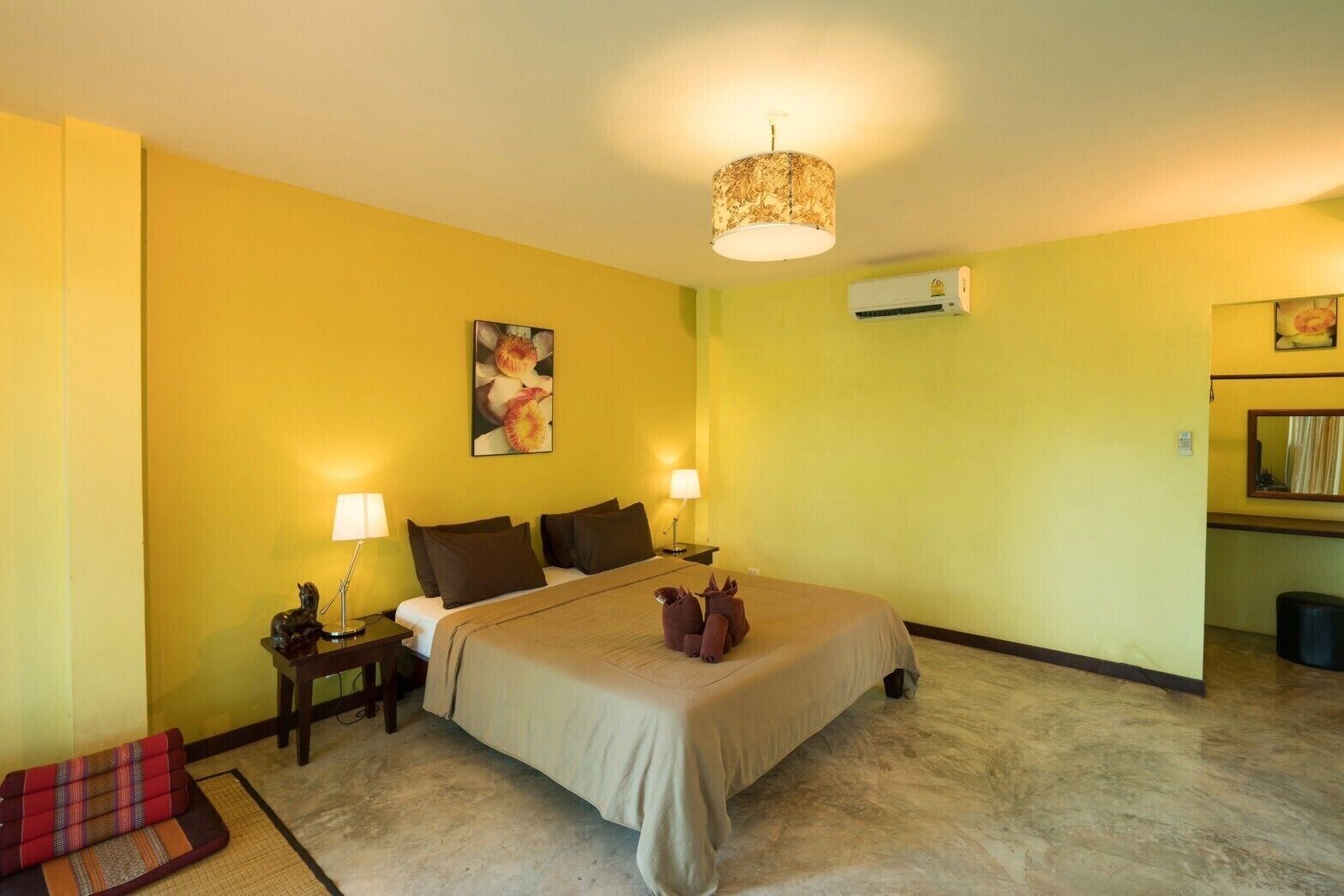 A hotel room with a bed, two bedside tables with lamps, a wall-mounted air conditioner, and a painting.