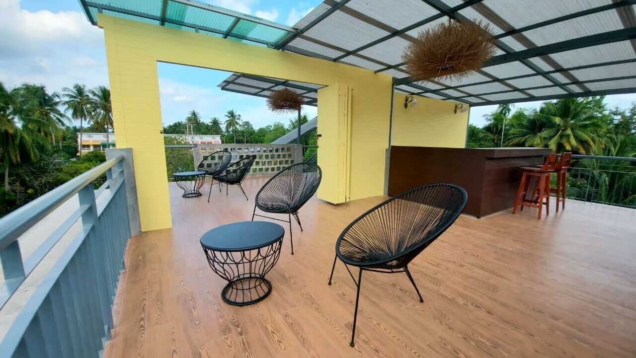 A covered outdoor seating area with wooden flooring and metal chairs, overlooking a lush green landscape.