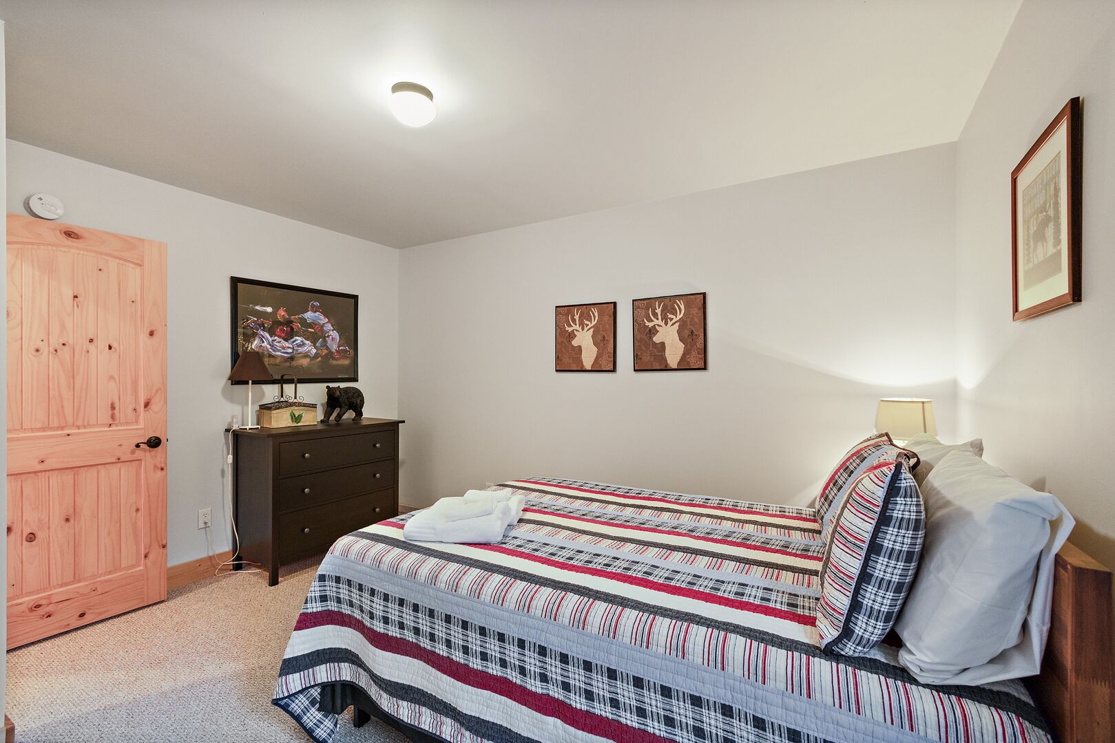 Een slaapkamer met een bed, een dressoir, een televisie en twee op de muur bevestigde hertenhoornschilderijen.