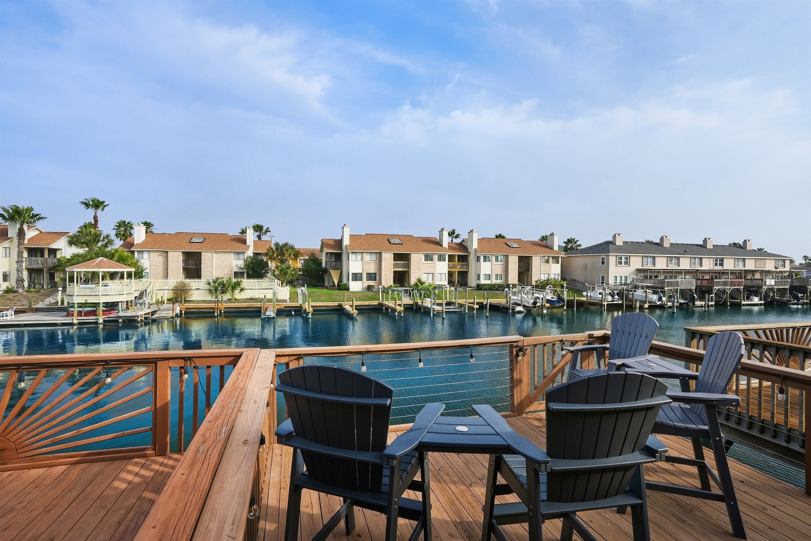 A wooden deck with Adirondack chairs overlooking a swimming pool and a marina.