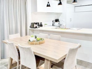 Une cuisine moderne avec des meubles blancs, une table à manger en bois et un petit îlot central doté d'une machine à café.
