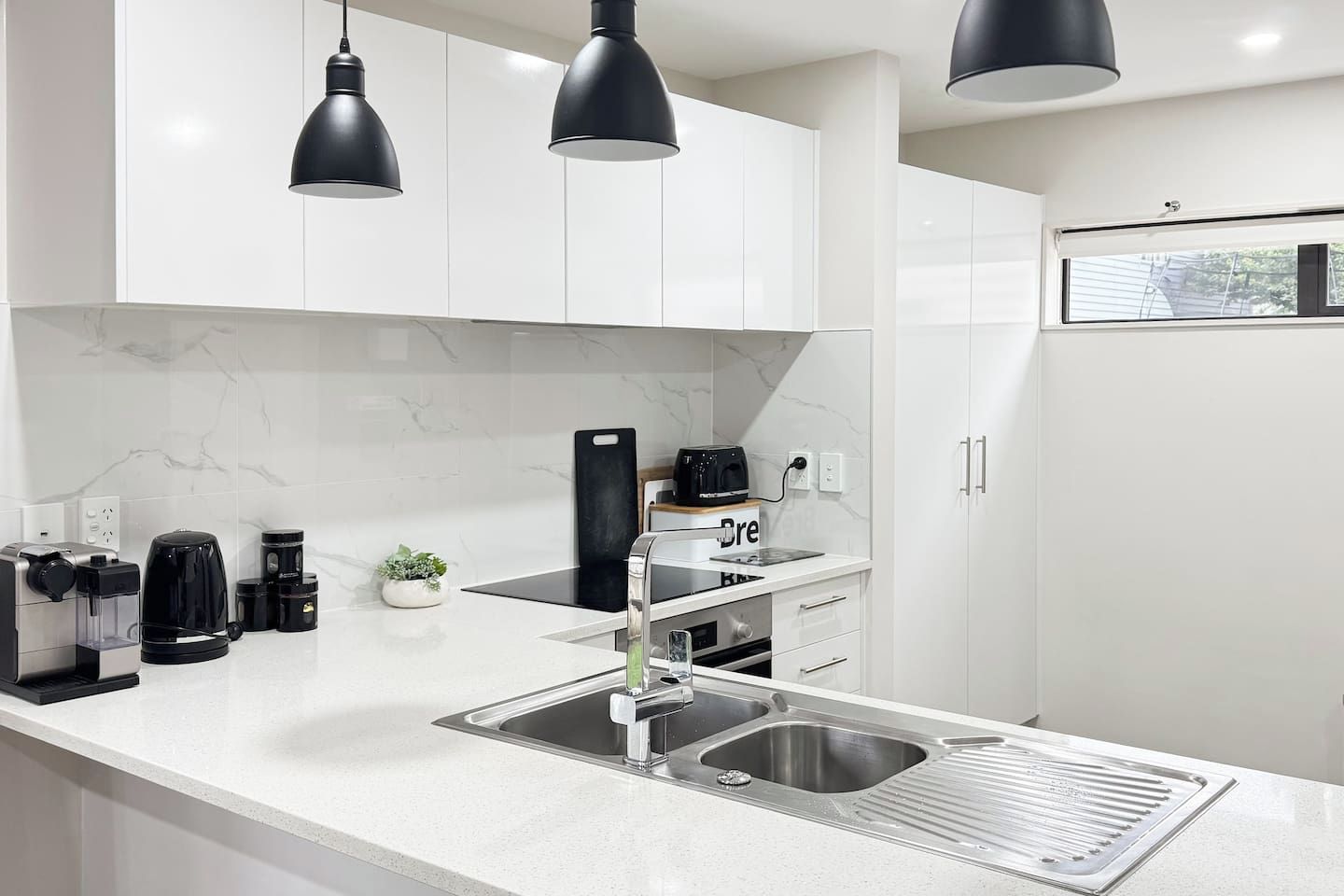 Een moderne keuken met witte kasten, een roestvrijstalen spoelbak en zwart hanglampen.