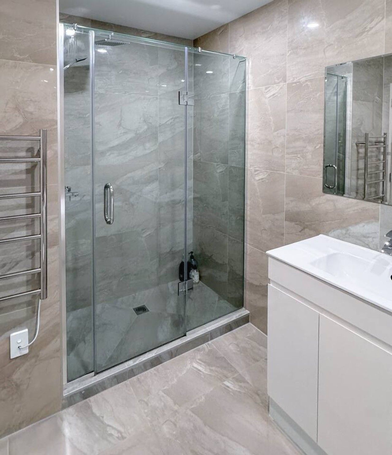 A modern bathroom with a glass-enclosed shower, a white vanity, and a large mirror.