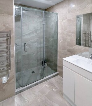 Un baño moderno con ducha envuelta en vidrio, tocador blanco y un espejo grande.