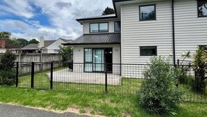 A two-story residential building with a fenced yard and a visible garage. - 3BR Home • Parking • Sleeps 6 • Near Transport (Panmure)