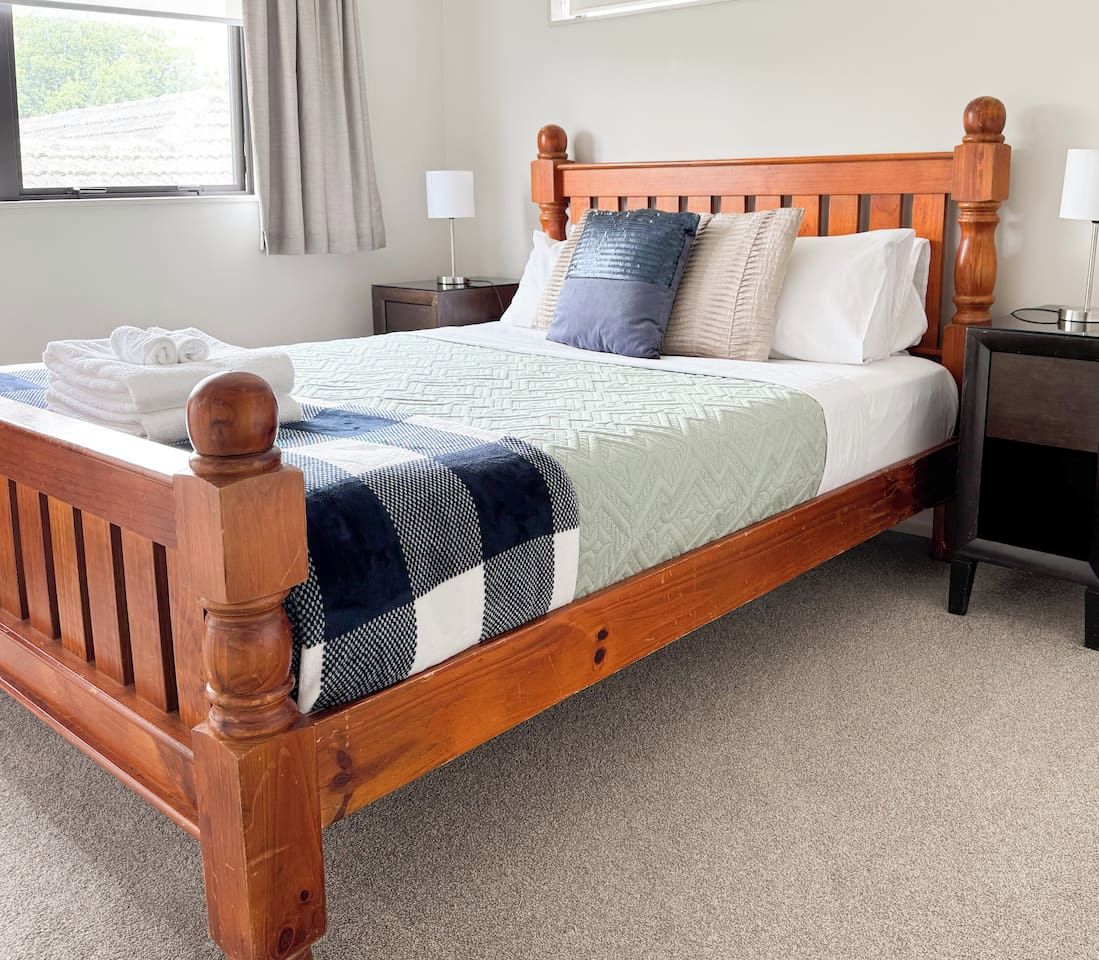A wooden bed with a quilt, pillows, and a bedside table.