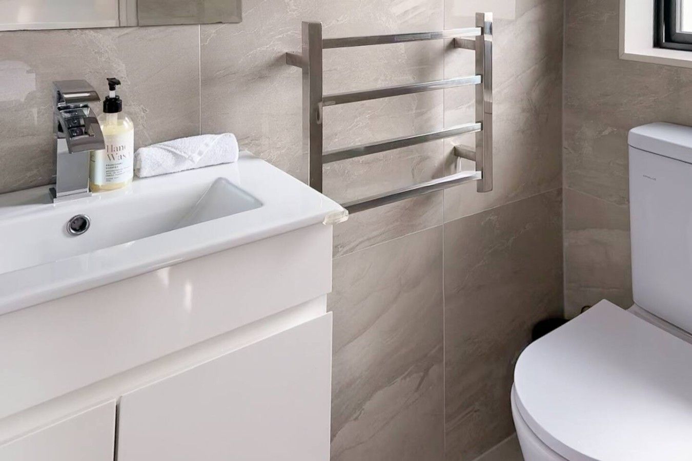 A modern bathroom with a white sink, toiletries, a towel rack, and a toilet.