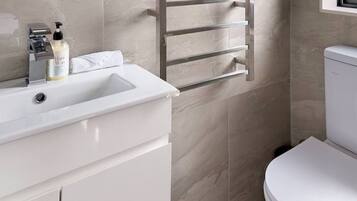 A modern bathroom with a white sink, toiletries, a towel rack, and a toilet.