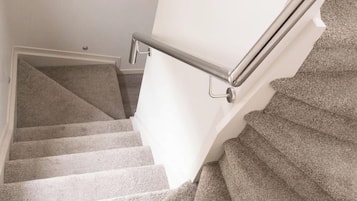A carpeted staircase with a metal handrail and a white wall.