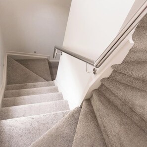 A carpeted staircase with a metal handrail and a white wall.