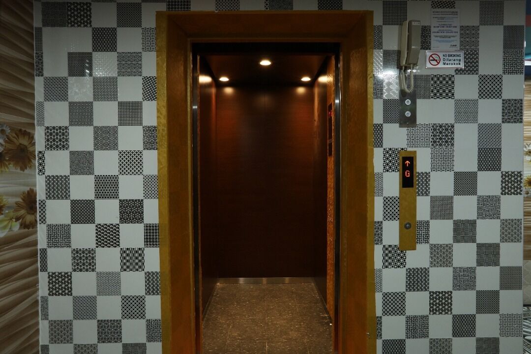 An elevator with a checkered tile wall, a wooden door, and a no-smoking sign.