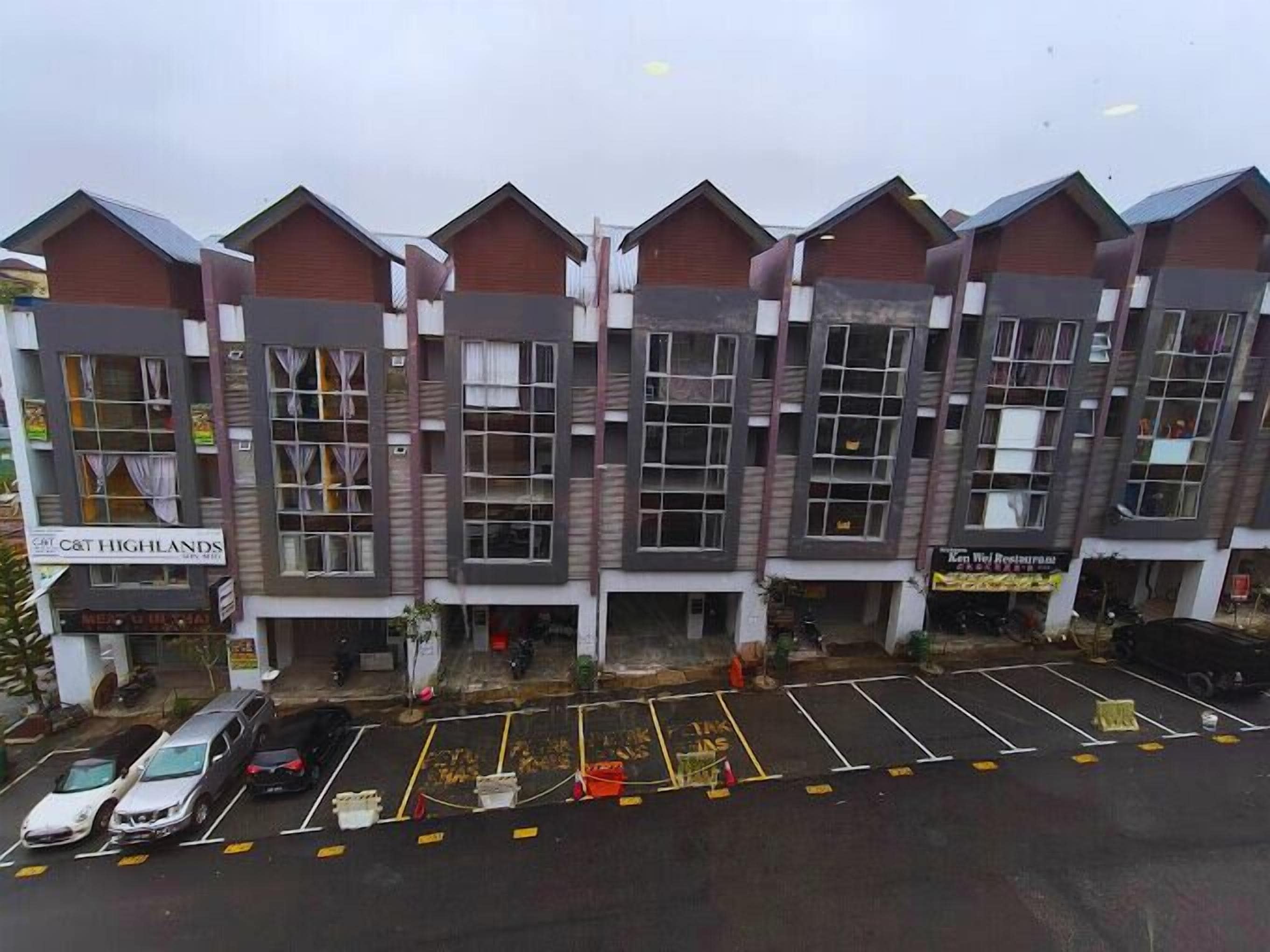 A multi-story building with a row of shops on the ground floor, including a restaurant. There is a parking lot in front with several cars parked.