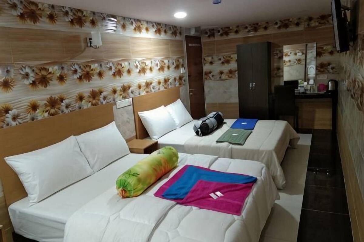 A hotel room with two beds, a desk, a mirror, and a wardrobe.