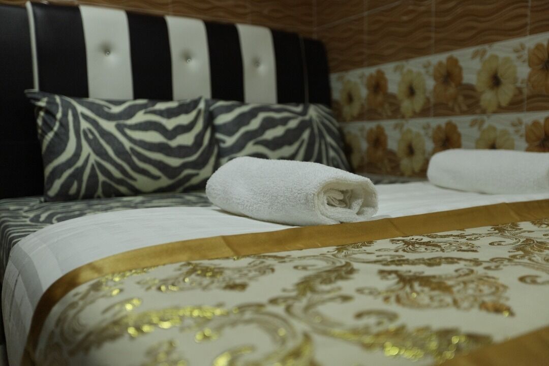 A hotel room with a striped headboard, zebra-patterned pillows, a rolled white towel, and a gold and white patterned bedspread.