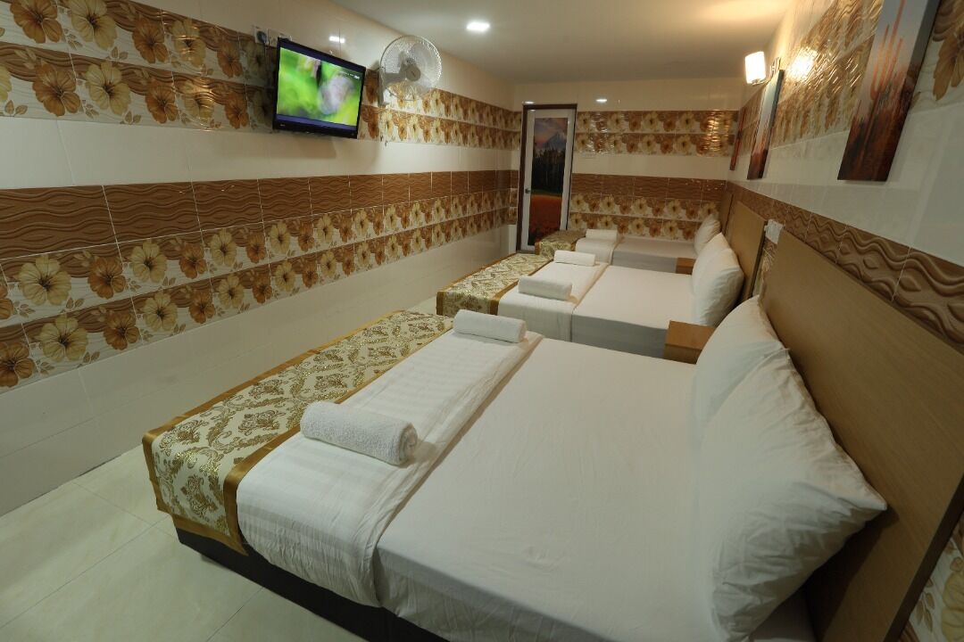 A hotel room with four single beds, a television, and a fan.