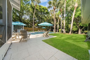 Un jardin avec une piscine, des chaises de patio et des parasols.