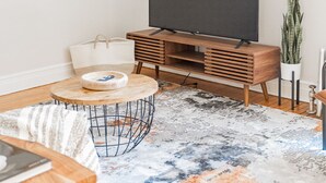 A modern living room with a flat-screen TV on a wooden stand, a round coffee table, a striped sofa, and a colorful abstract rug. - Vintage Escape 1BR Two Blocks Away From Beach (Chicago)