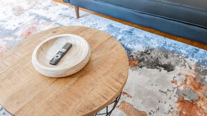 A remote control on a round wooden table in a living room with a blue sofa and a colorful rug. - Vintage Escape 1BR Two Blocks Away From Beach (Chicago)